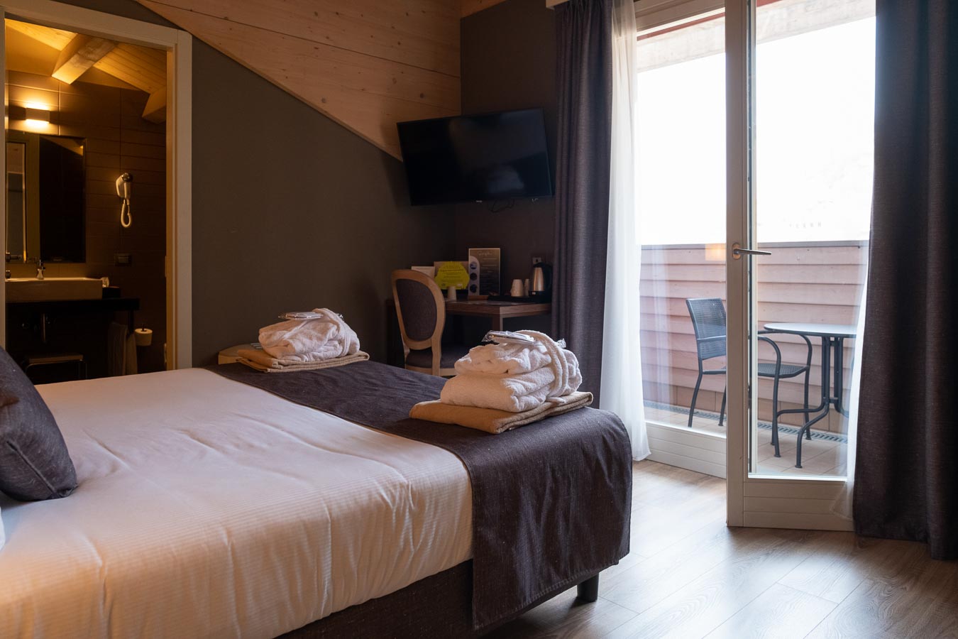 Camera d'hotel accogliente con letto matrimoniale, accappatoi, vista sul balcone e bagno aperto.