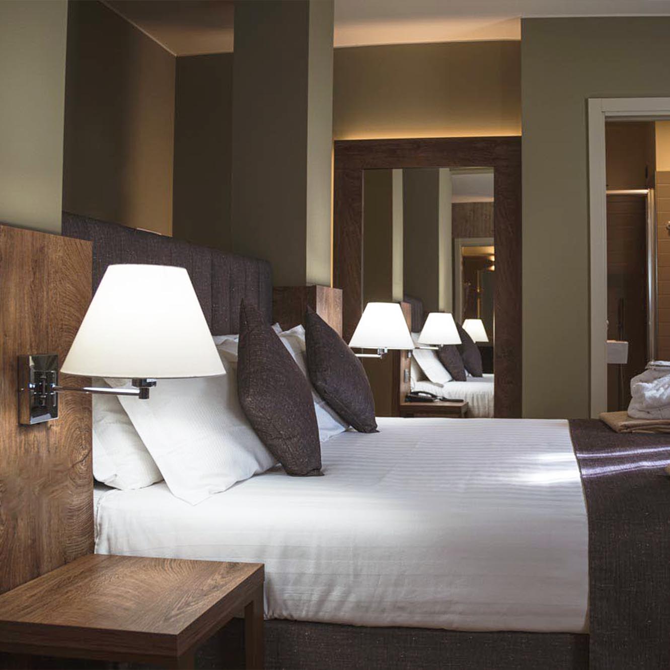 Camera d'albergo moderna con letto matrimoniale, cuscini scuri e lampada da lettura.