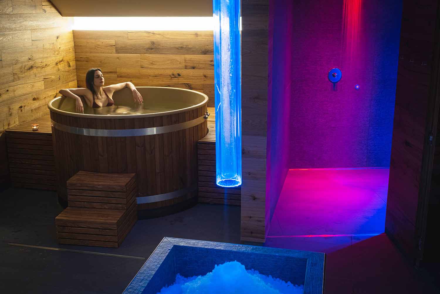 Una donna si rilassa in una vasca rotonda in una spa con illuminazione ambientale colorata.