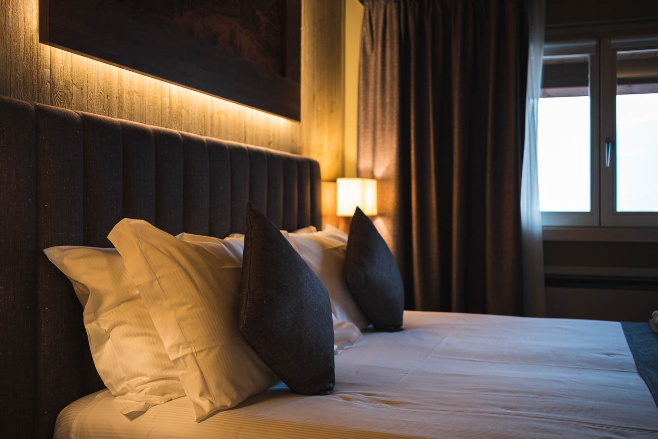 Letto matrimoniale con cuscini e illuminazione soffusa in una camera accogliente.