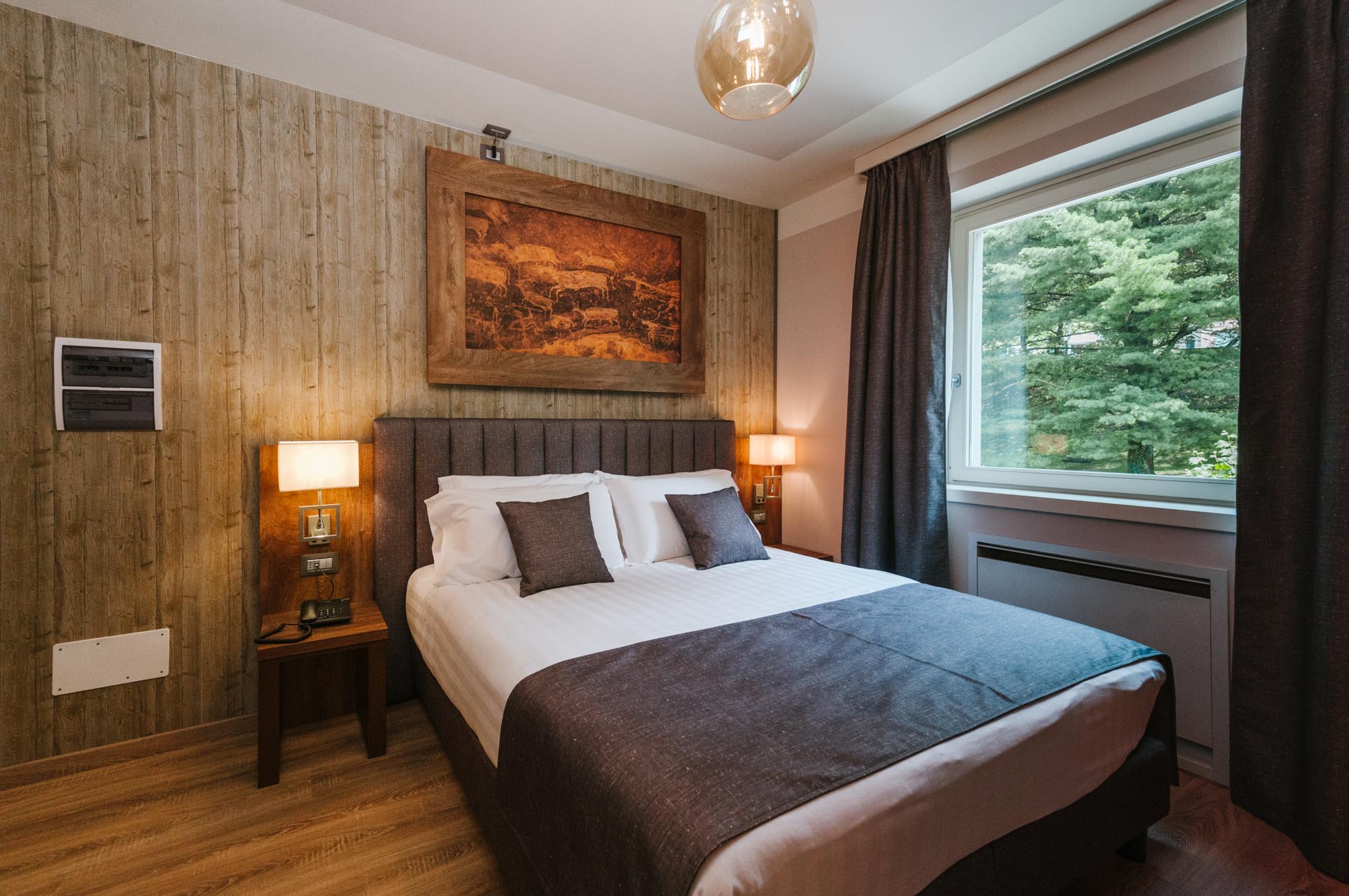 Camera da letto accogliente con letto matrimoniale, decorazione murale e finestra con vista su alberi.