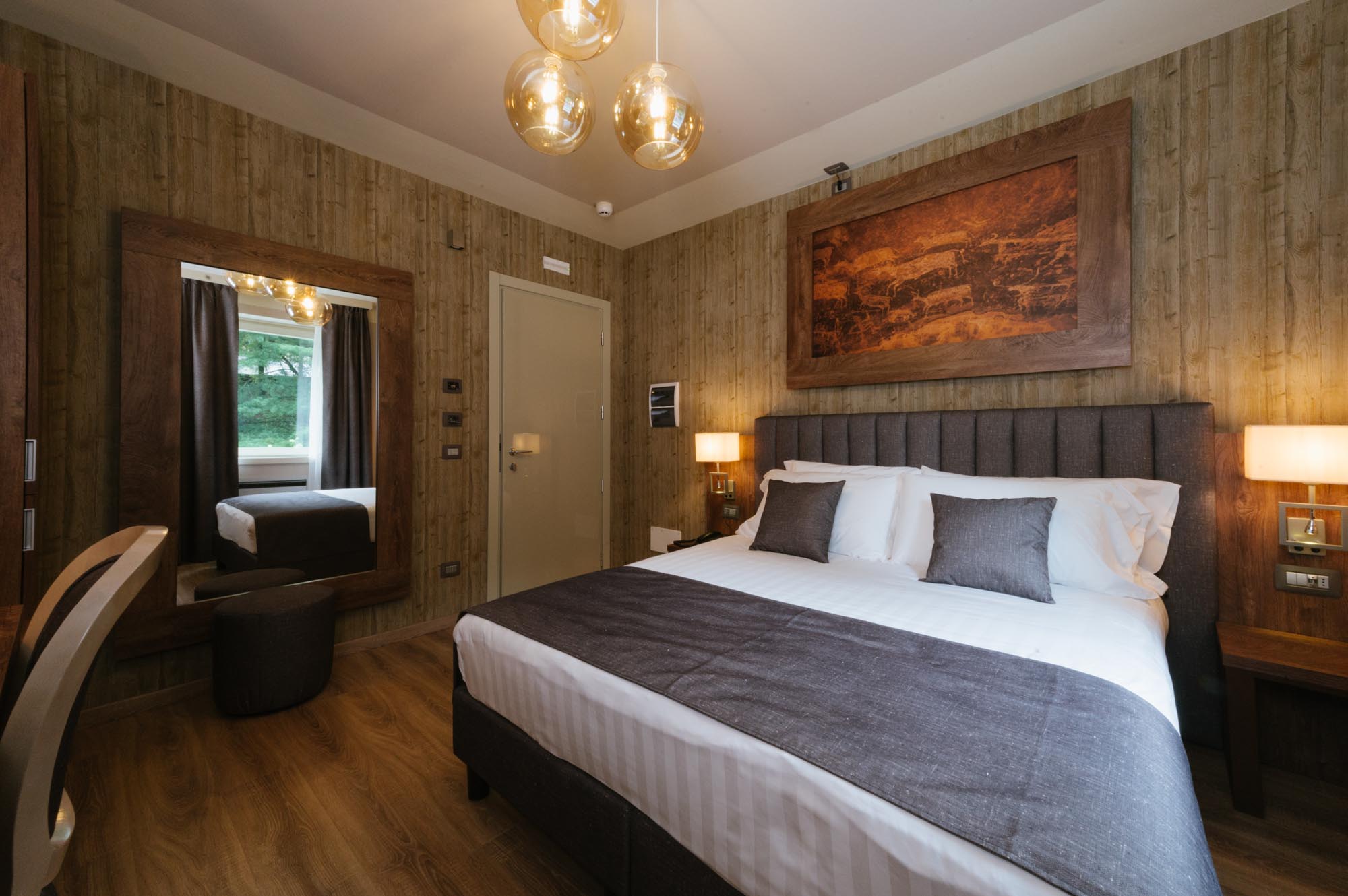 Camera da letto moderna con letto matrimoniale, lampade sospese e arredamento in legno naturale.