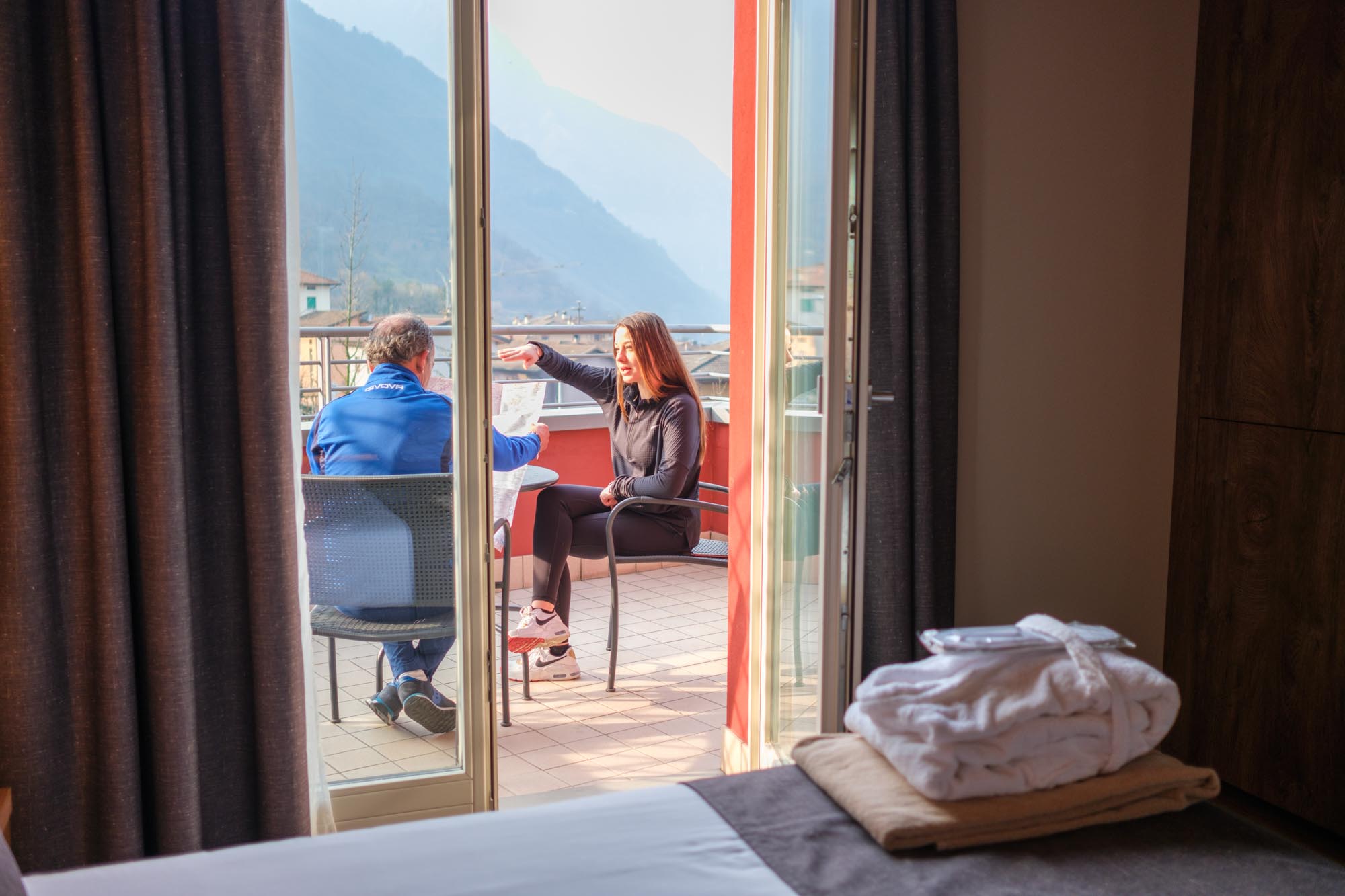 Due persone conversano su un balcone con vista sulle montagne.