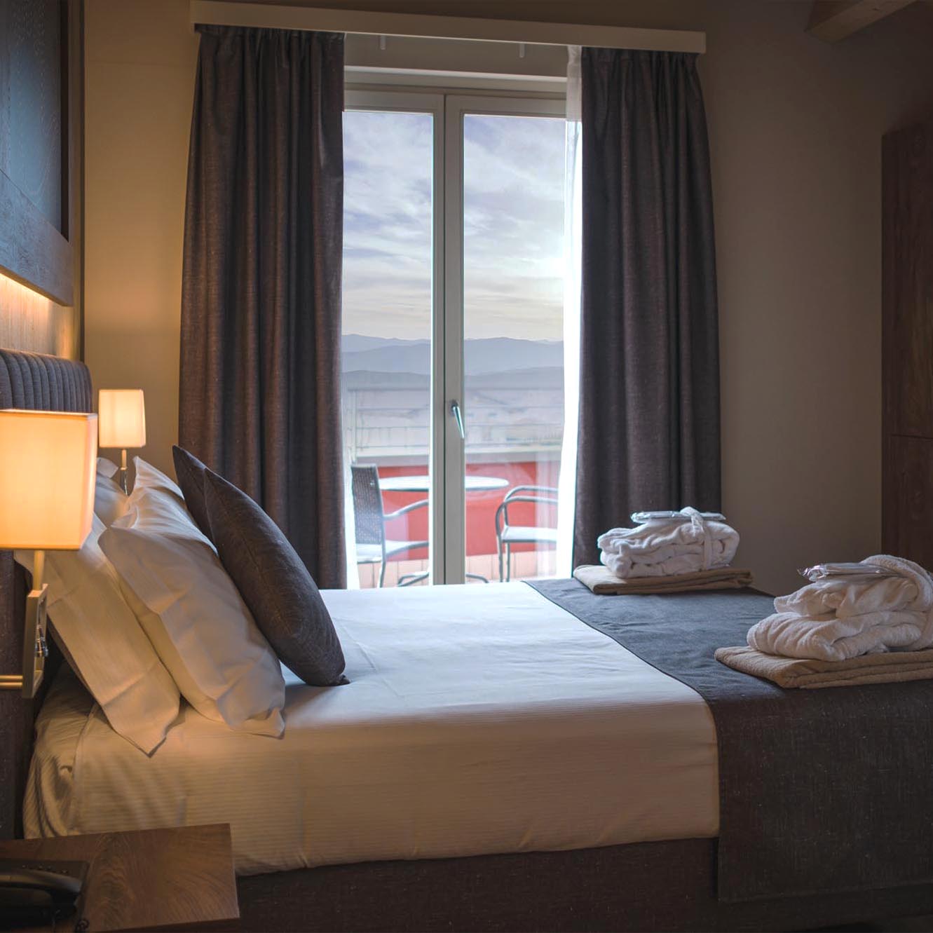 Camera d'albergo accogliente con letto matrimoniale, grandi finestre e vista sulle montagne.