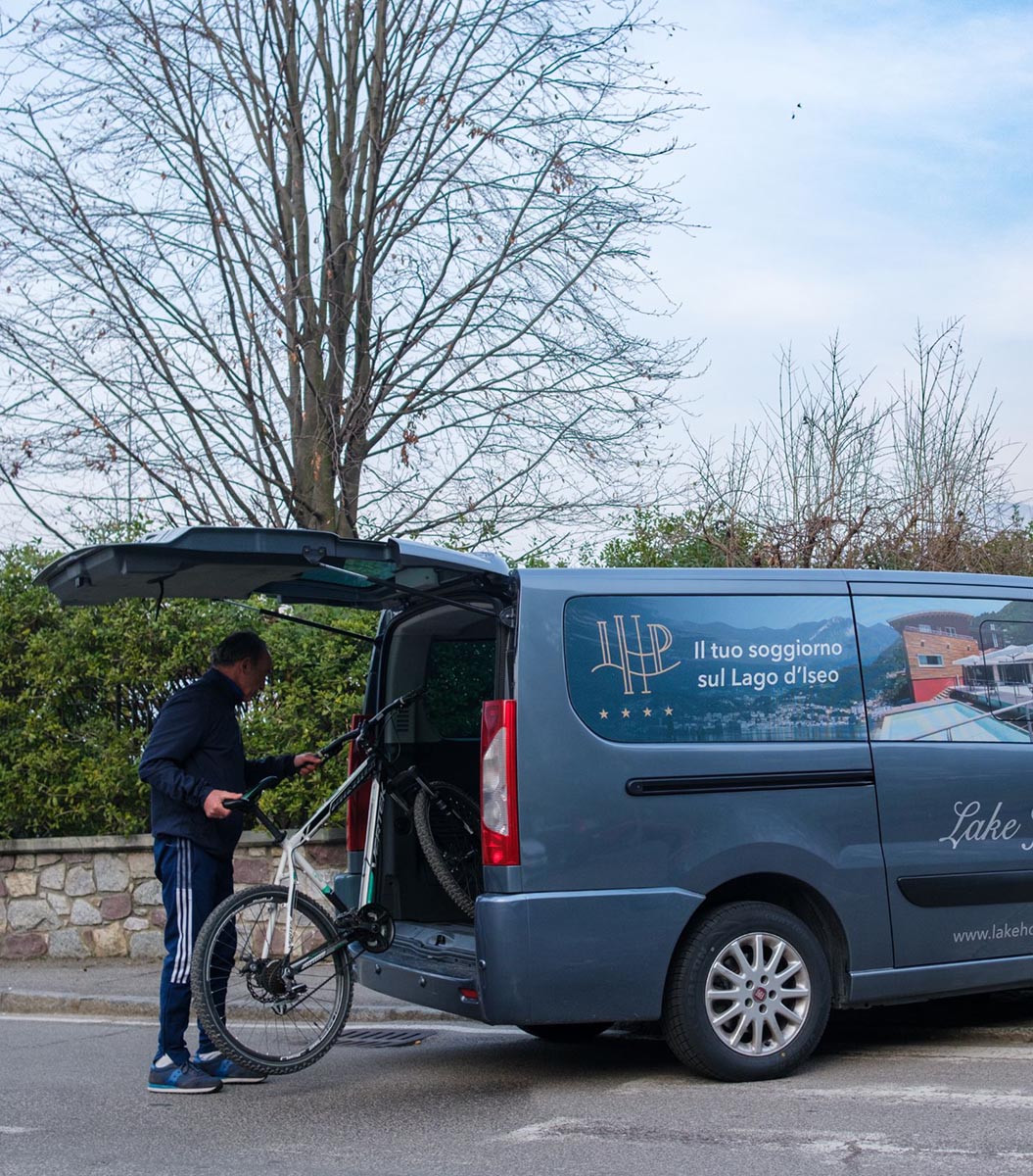 Un homme charge un vélo dans le coffre d'une camionnette bleue stationnée.