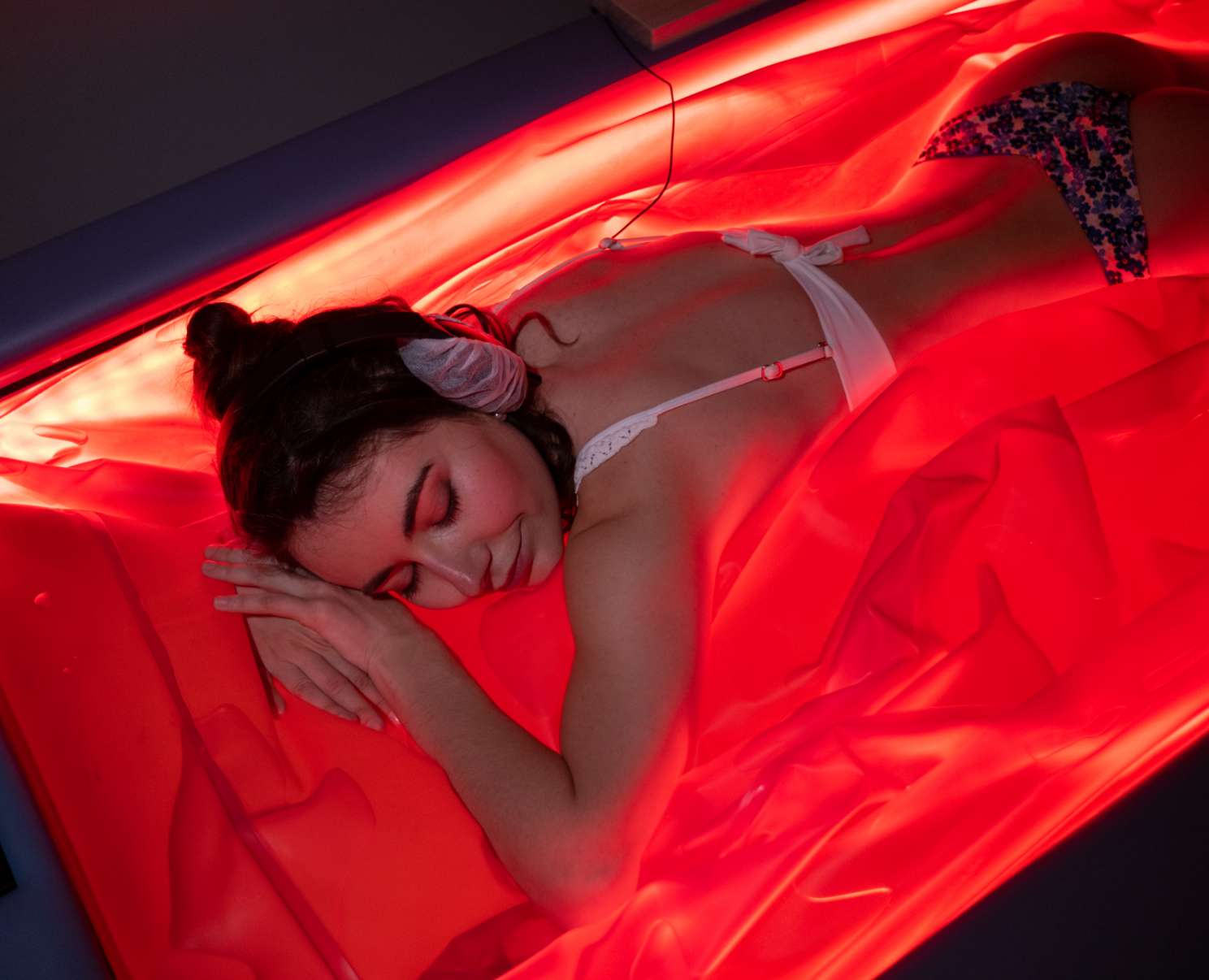Une femme se détend avec un casque audio dans un bain flottant lumineux rouge.