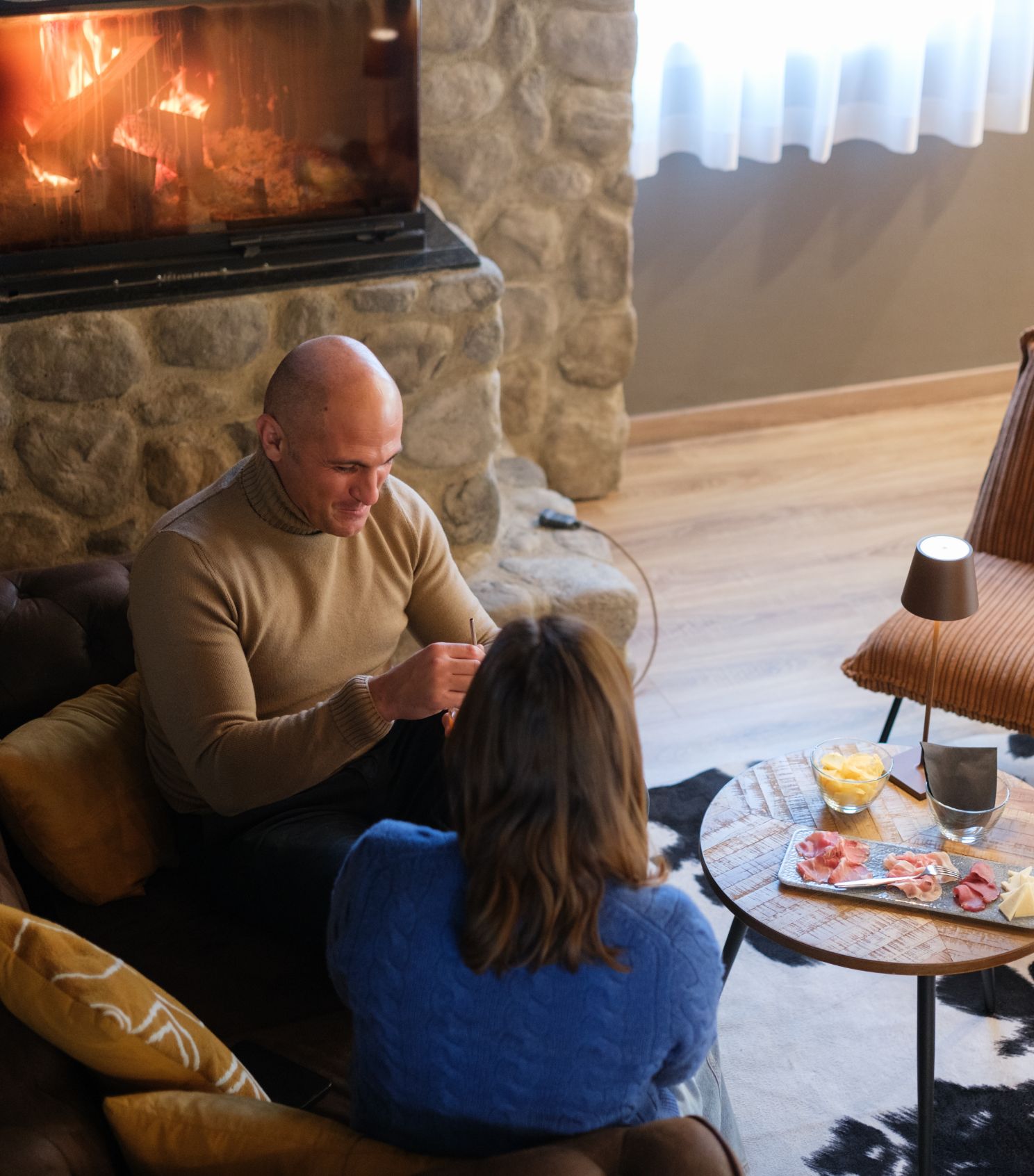 Due persone conversano davanti a un camino acceso in un'accogliente sala da pranzo.