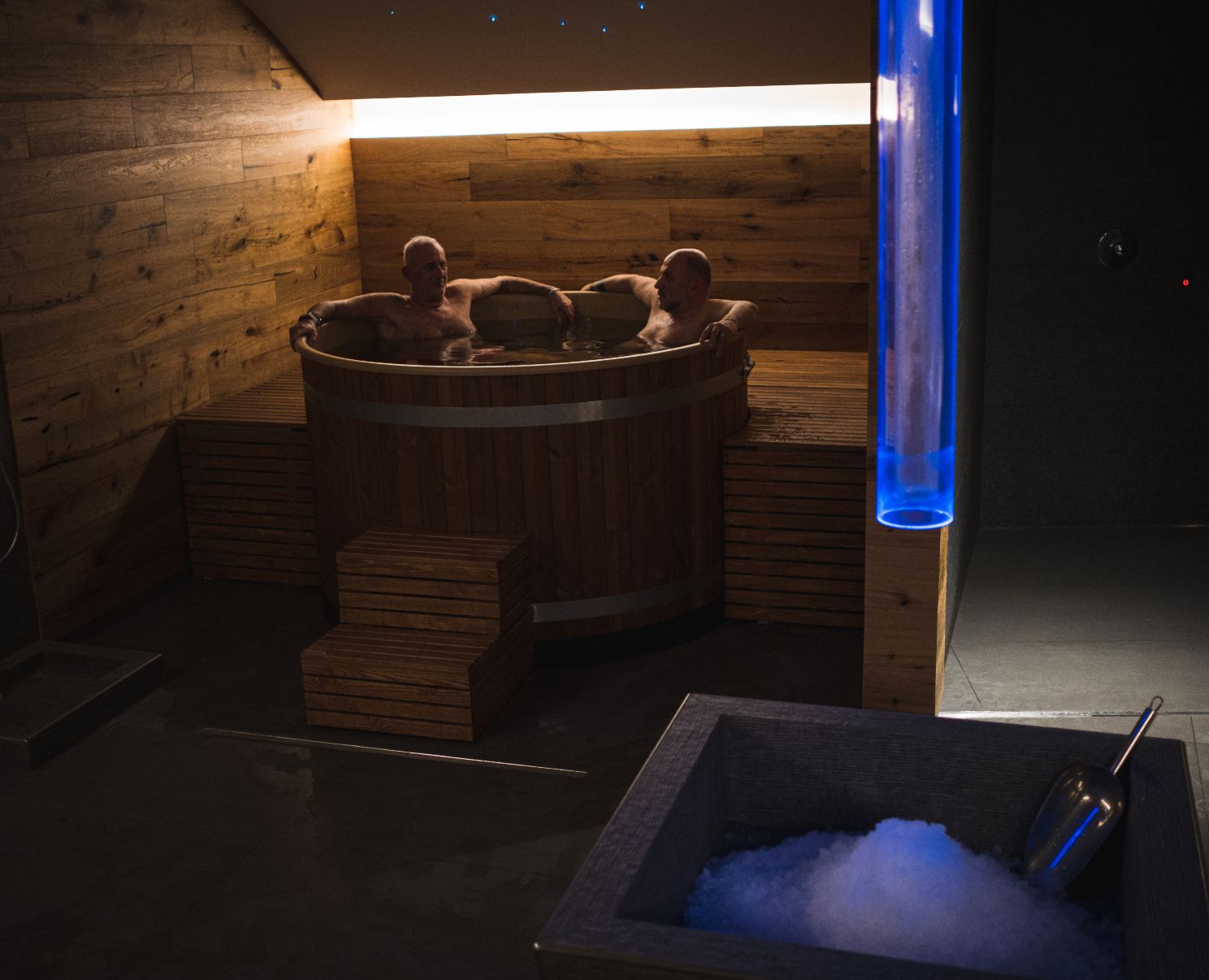 Due persone rilassano in una vasca di legno in una spa con illuminazione soffusa.