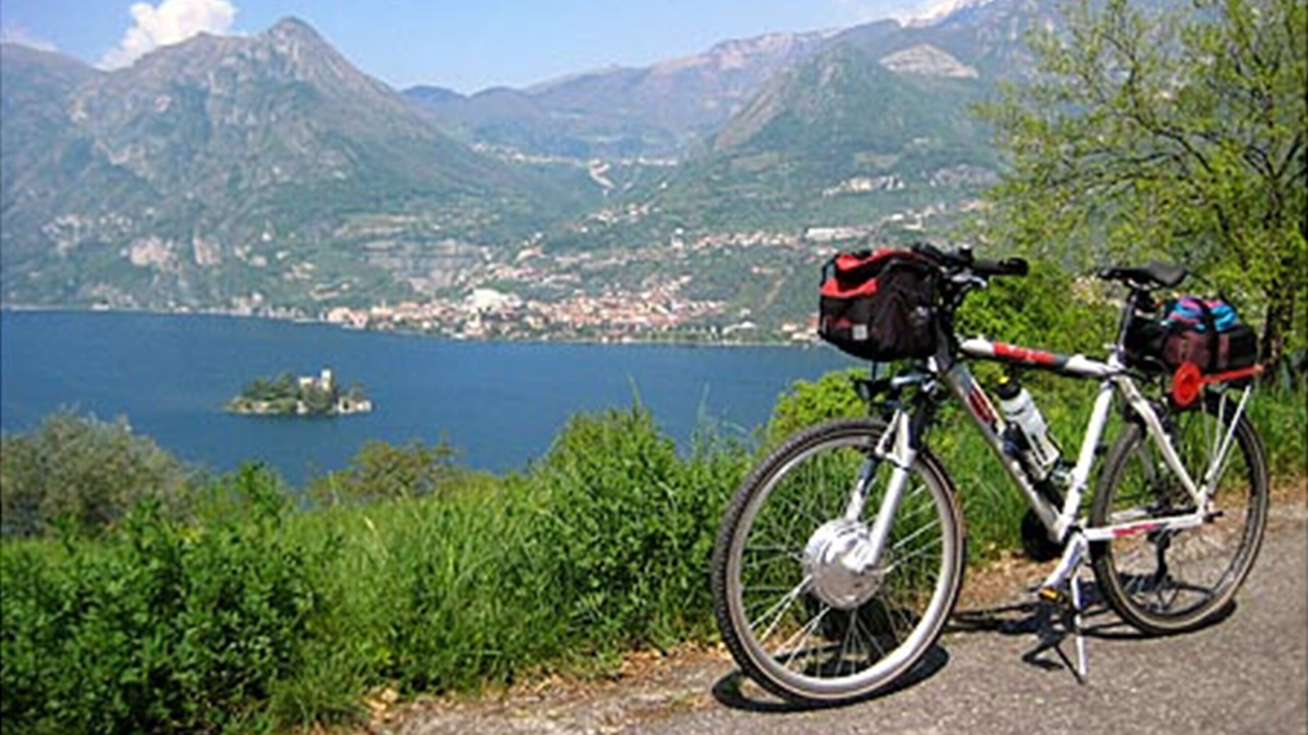 Bicicletta parcheggiata su un sentiero panoramico con vista su un lago e montagne.