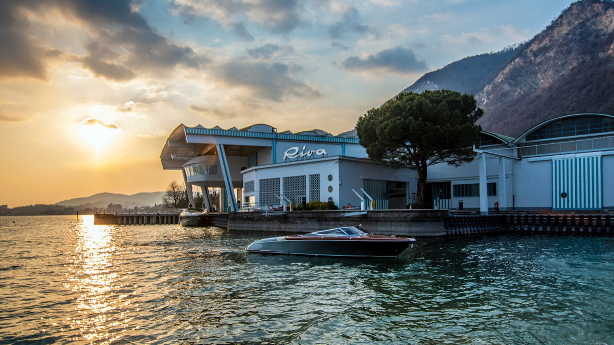Tramonto su un edificio moderno lungo un lago con una barca in primo piano.