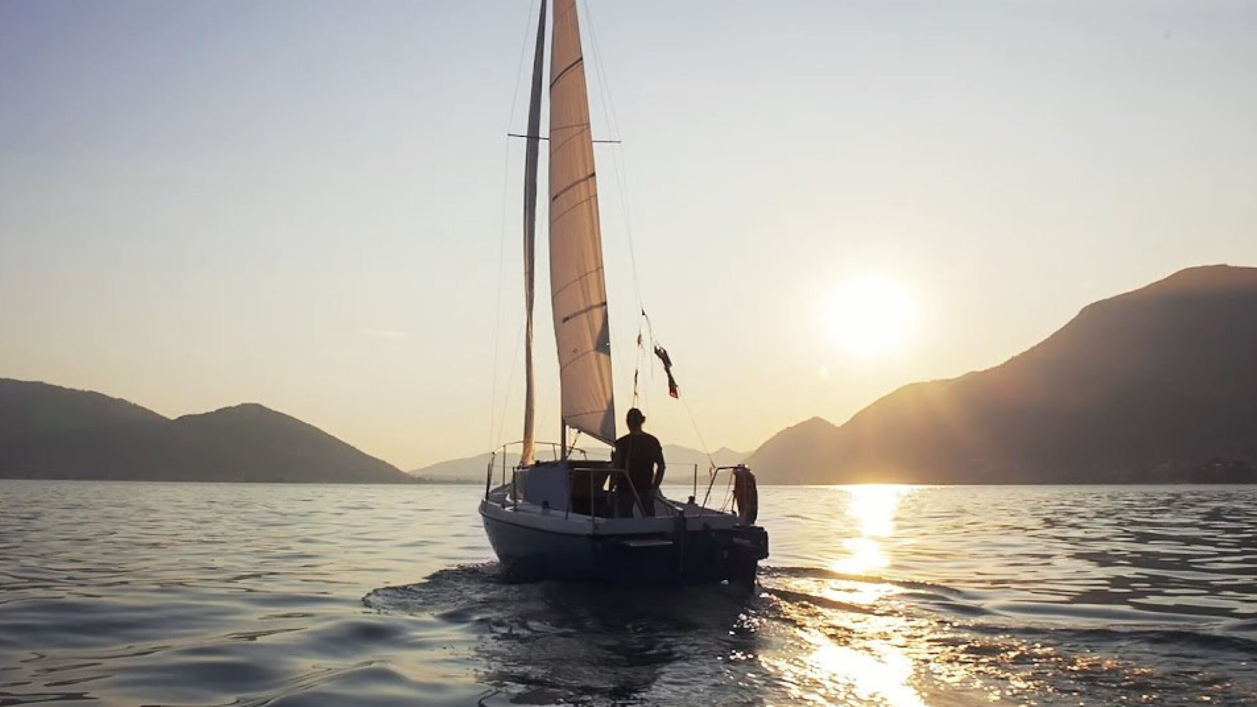 Barca a vela al tramonto su un lago circondata da montagne.