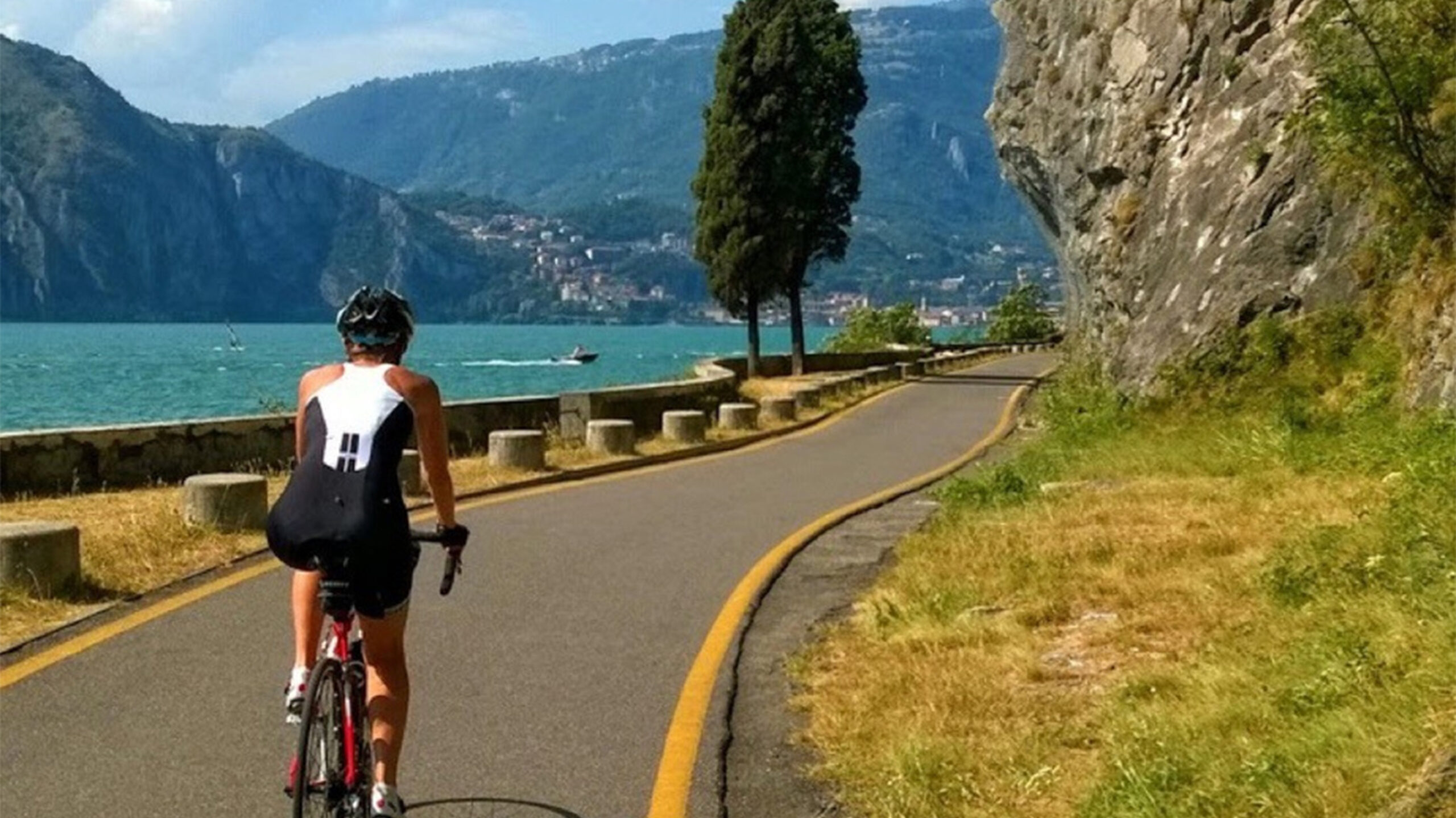 Un ciclista percorre una strada panoramica lungo un lago circondato da montagne.