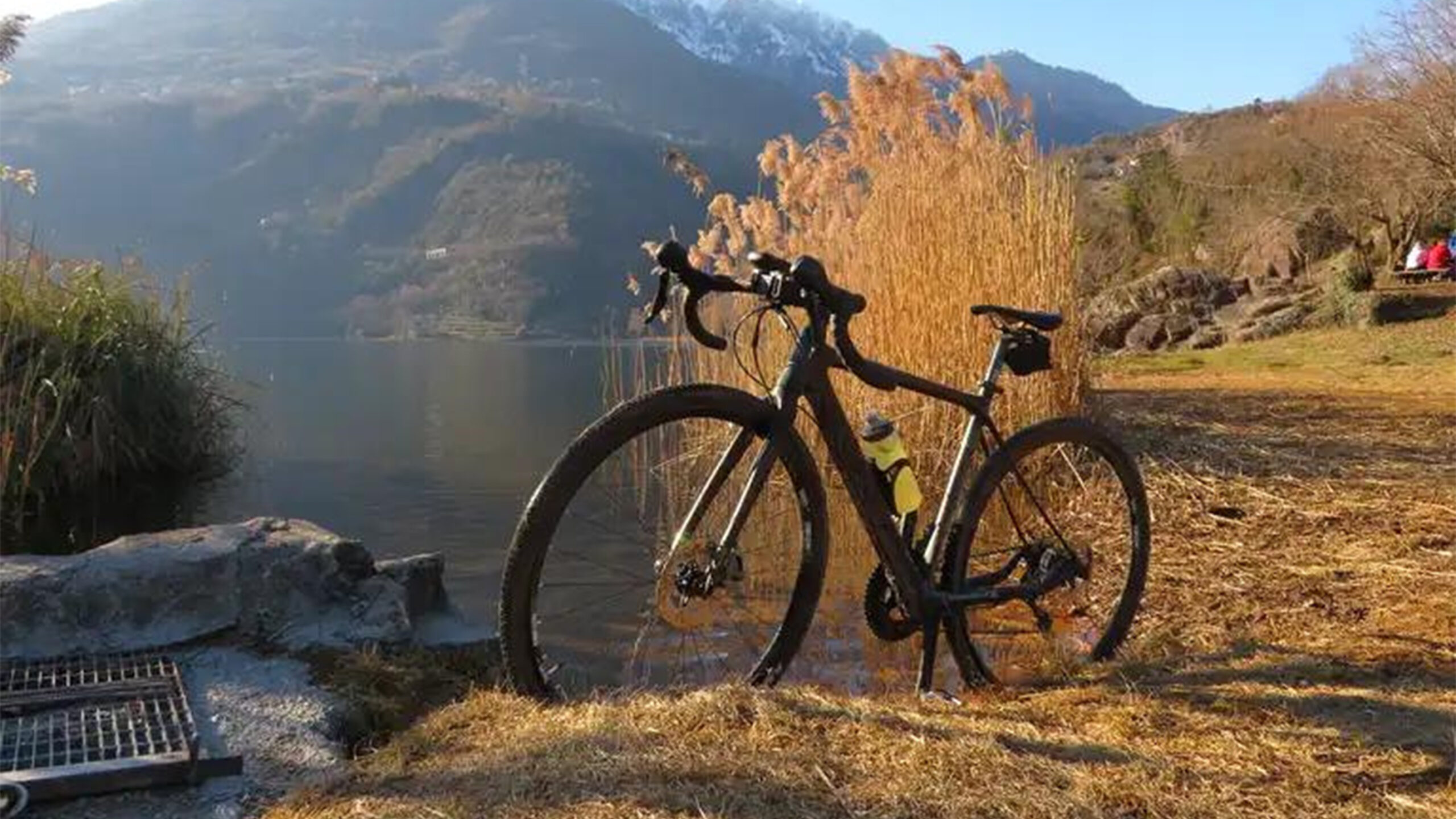 Bicicletta nera parcheggiata vicino a un lago con sfondo montano.
