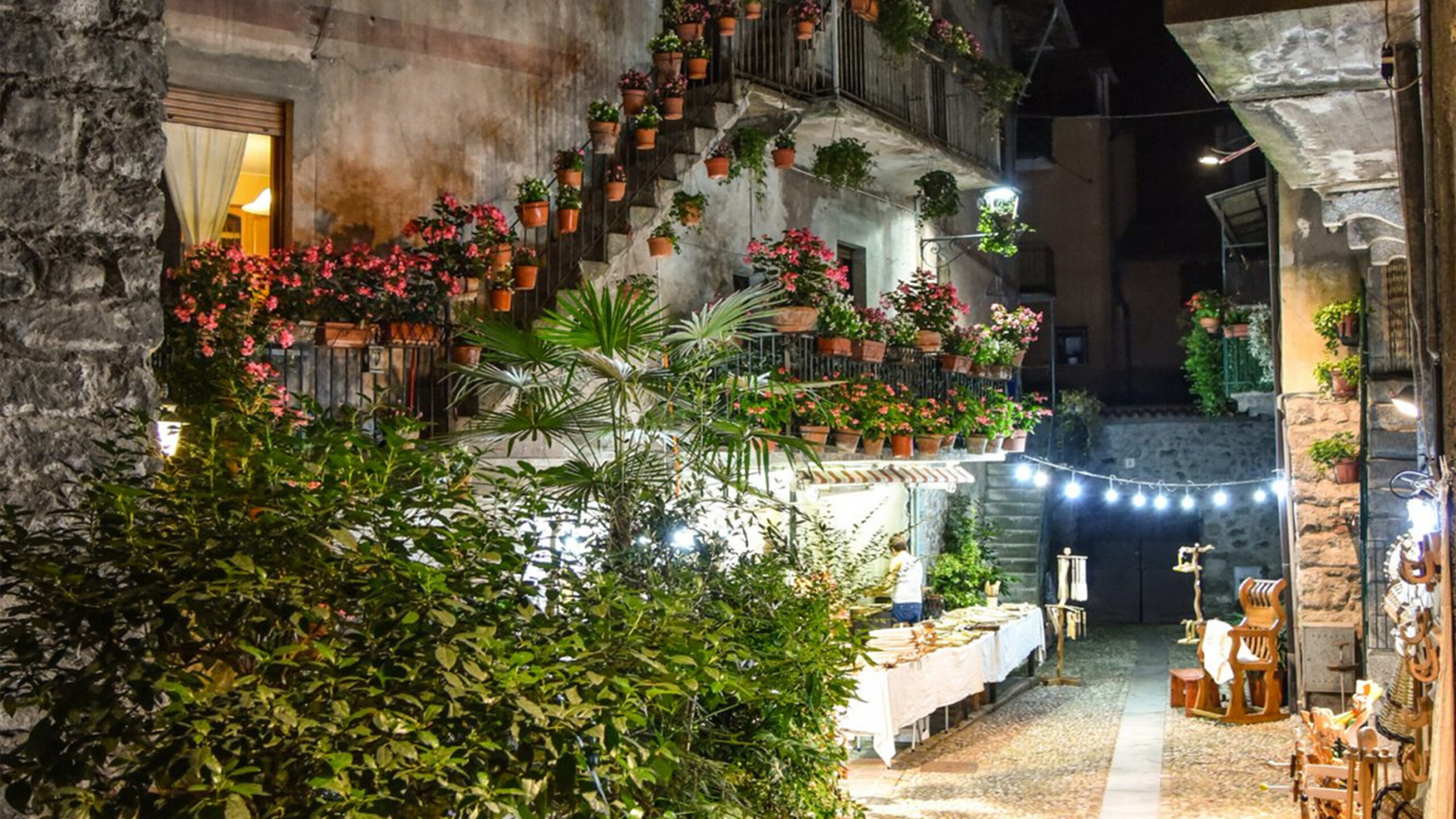 Stradina notturna di un villaggio italiano decorata con piante e lucine.