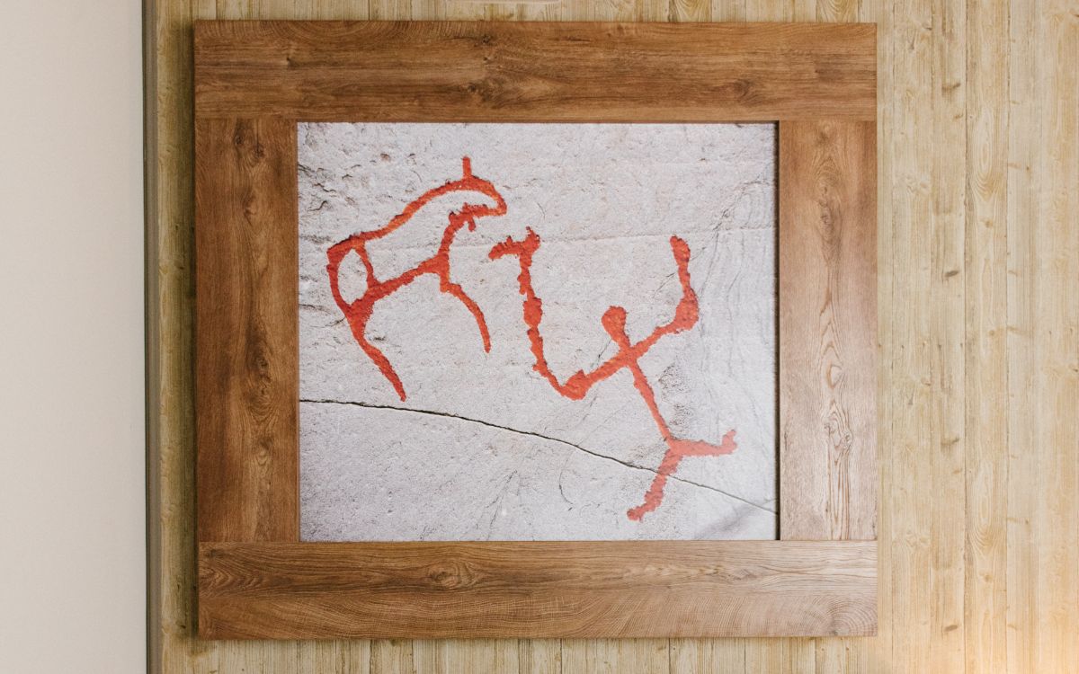 Quadro con pittura rupestre rossa raffigurante una figura umana e un animale su sfondo di pietra.