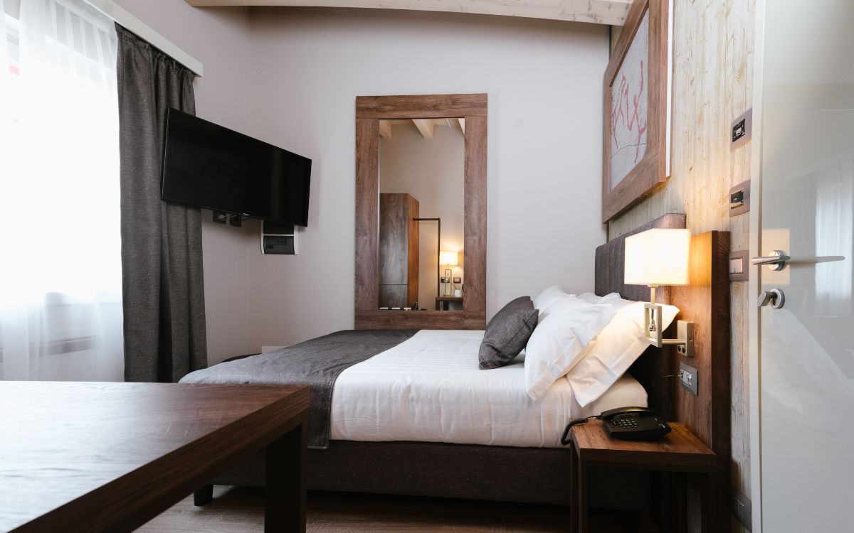 Camera da letto moderna con letto matrimoniale, specchio grande, televisore e lampada da comodino.