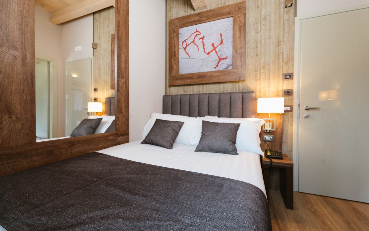 Camera da letto moderna con letto matrimoniale, lampade accese e grande specchio.