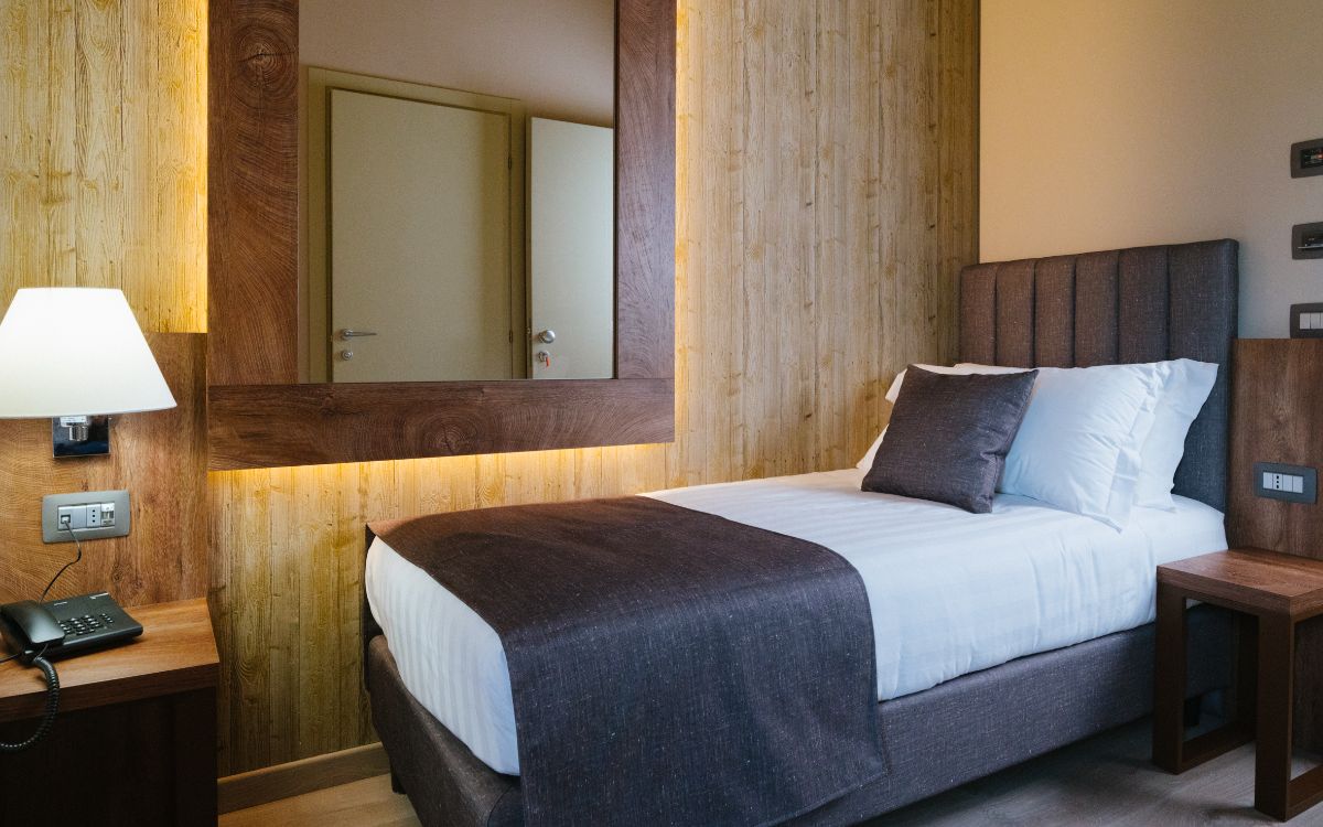 Camera d'albergo moderna con letto singolo, specchio grande e testiera imbottita.