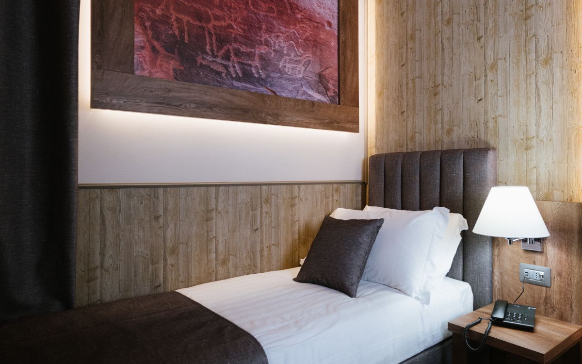 Camera d'albergo accogliente con letto singolo e lampada da comodino.